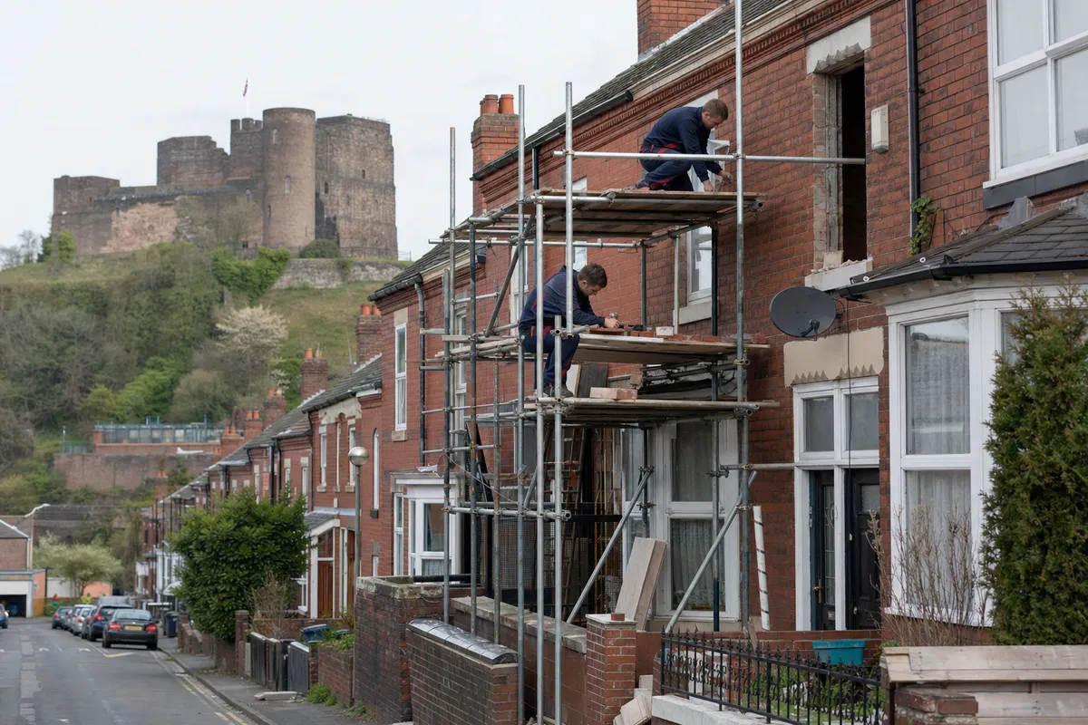 Builder repointing brickwork on a terraced house in Dudley with the castle hill behind